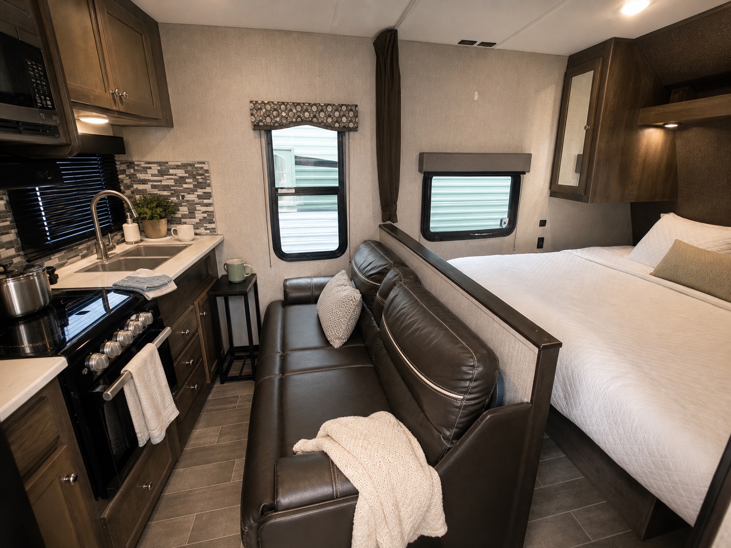 Staged Coleman Lantern trailer interior with clean bedding, lounge seating, and compact kitchen